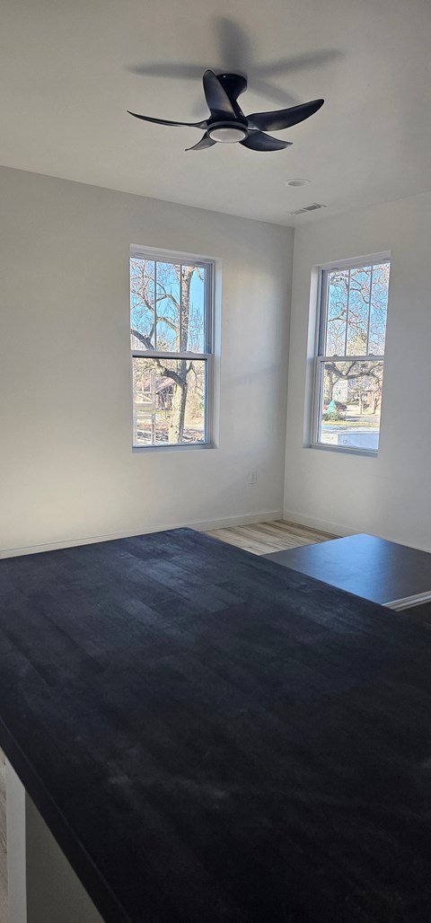 A room with a ceiling fan and two windows.
