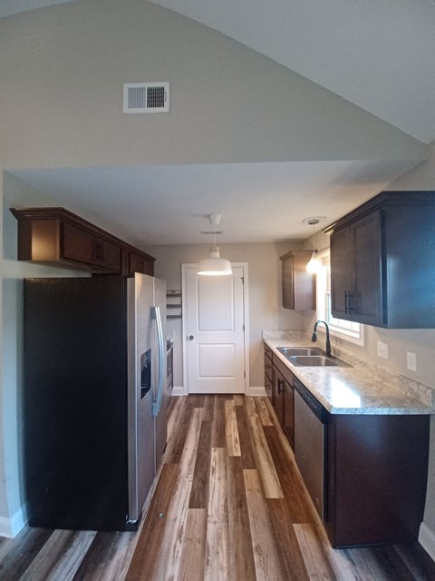 A kitchen with a black refrigerator and wooden floors.