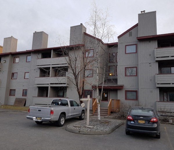 A silver truck is parked in front of a grey building.