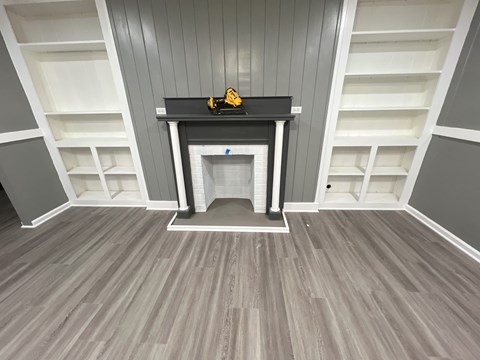 A black shelf with a yellow object on it is in the middle of a room with grey walls and a grey floor.