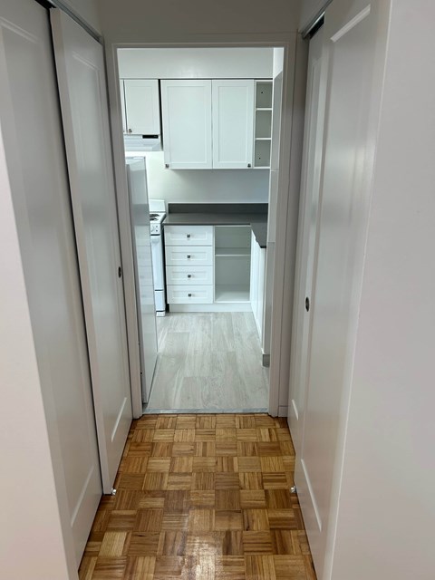 A hallway with a wooden floor leads to a kitchen.