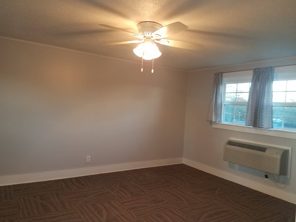 A room with a ceiling fan and a window with a curtain.