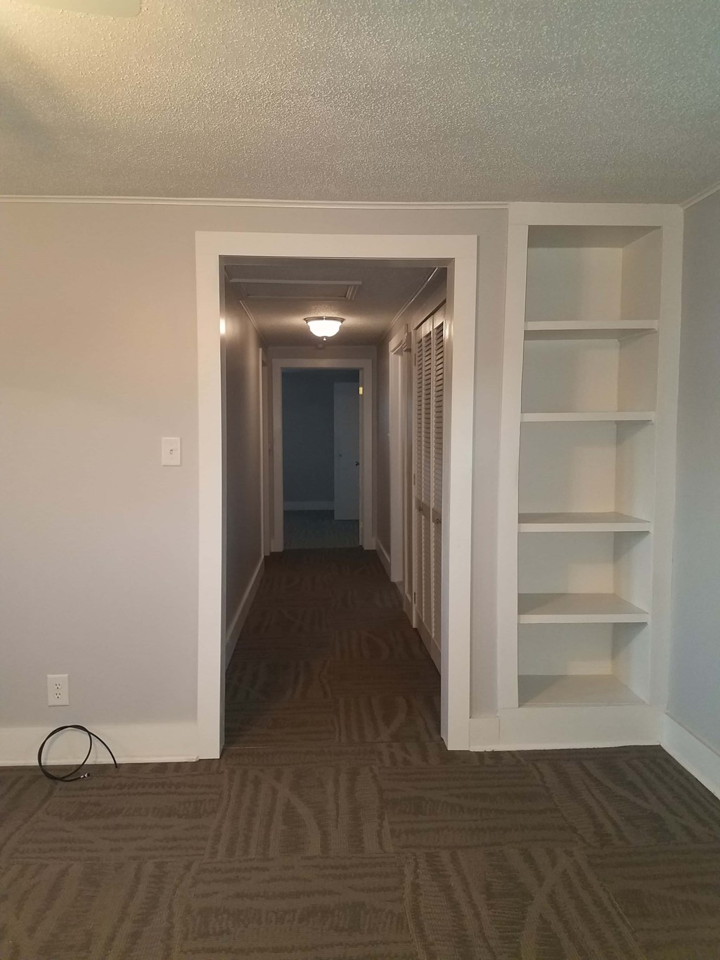 A hallway with a door at the end and a carpet on the floor.