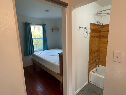 A bedroom with a bed, a window with blue curtains, and a wooden wall.