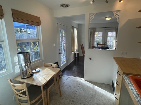 A kitchen with a table and chairs in the foreground and a hallway leading to a door in the background.