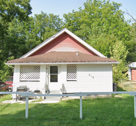 A small white house with a red roof and a porch.