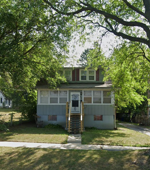 A small house with a porch and a tree in front.