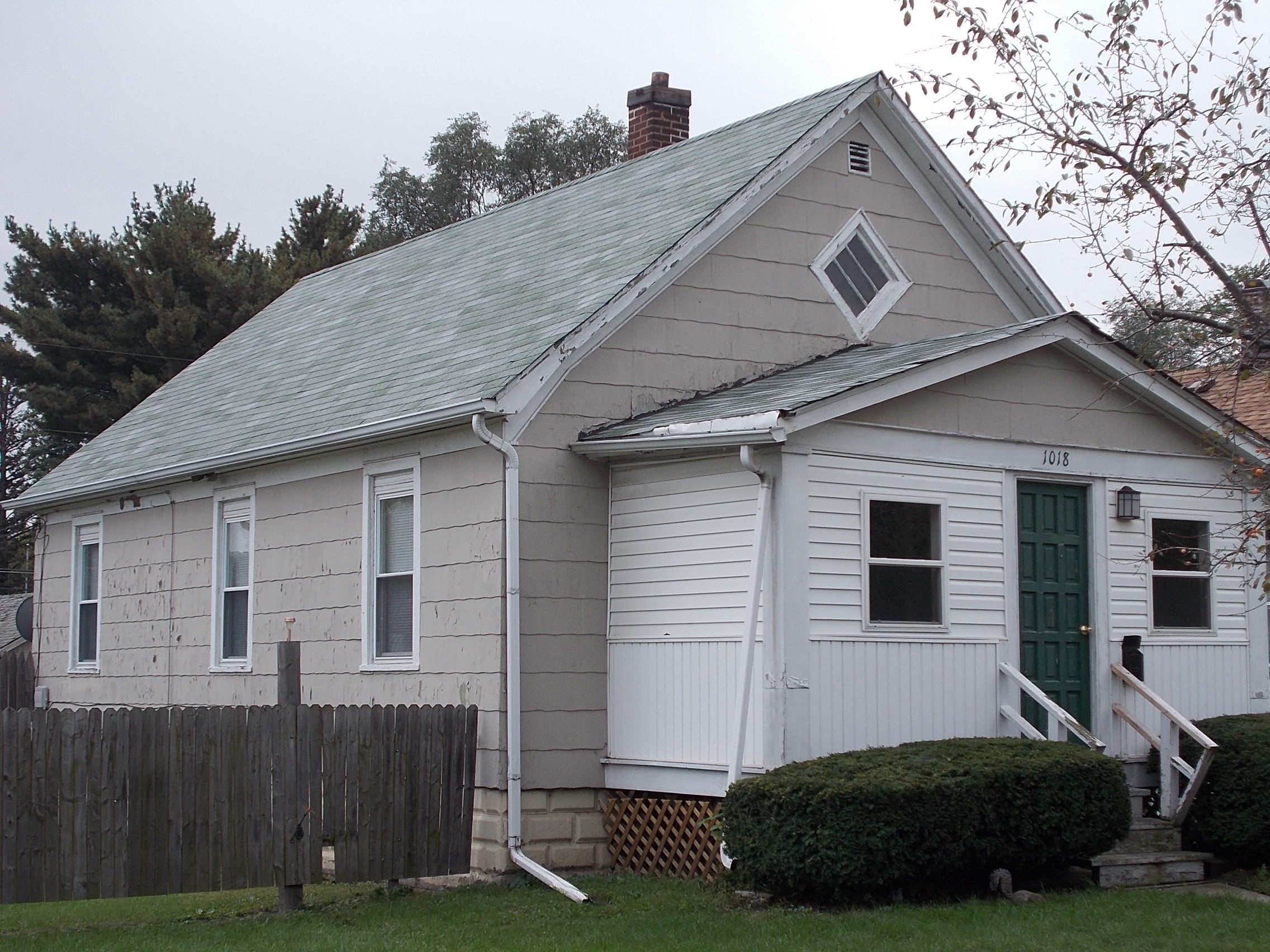 A small white house with a green door and a wooden fence.