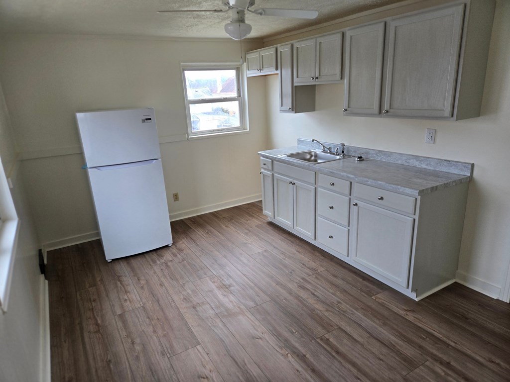 A kitchen with a white fridge and wooden floors.