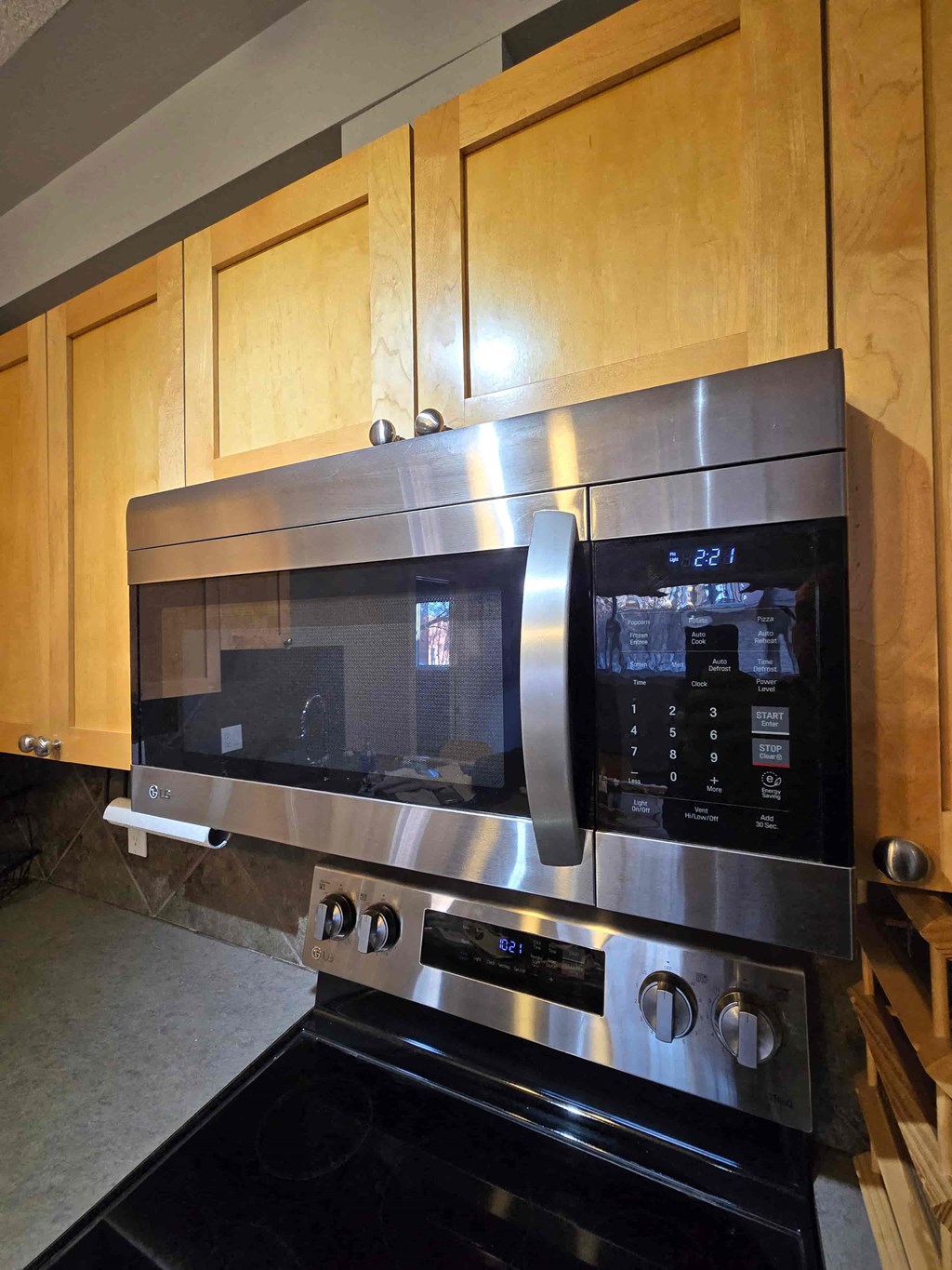A stainless steel microwave oven with digital display and control panel is installed above a stove.