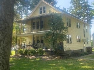 A yellow house with a porch and a tree in front.