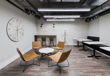 A large clock hangs on the wall above a table with chairs around it.