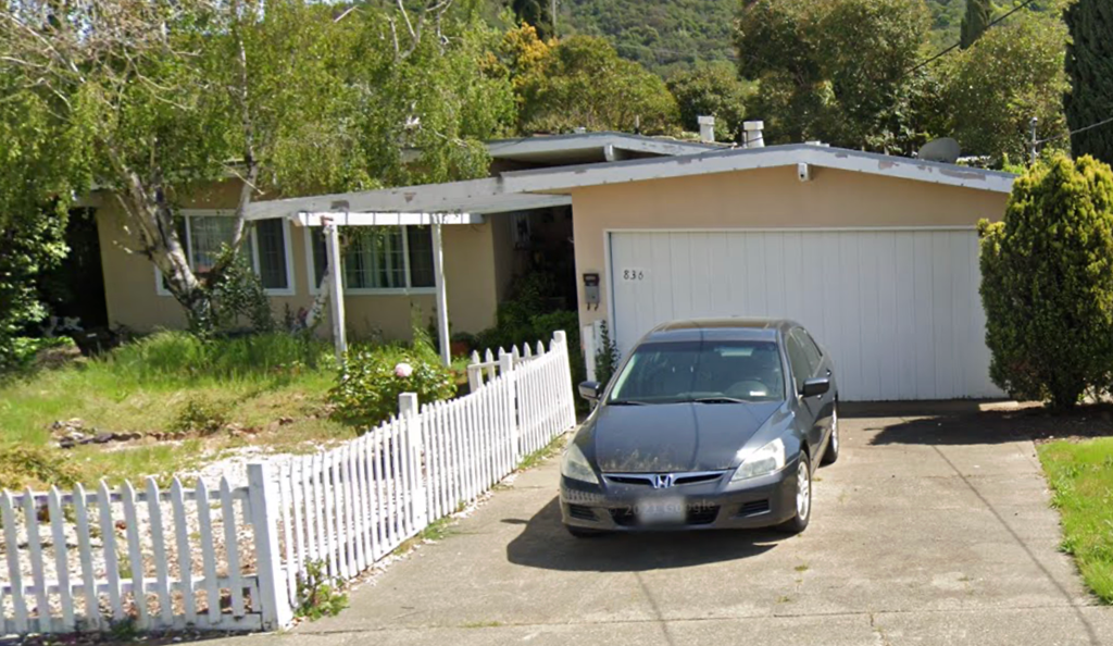 A silver Honda car is parked in front of a white picket fence and a house.