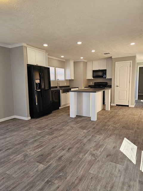 A kitchen with black appliances and wooden flooring.