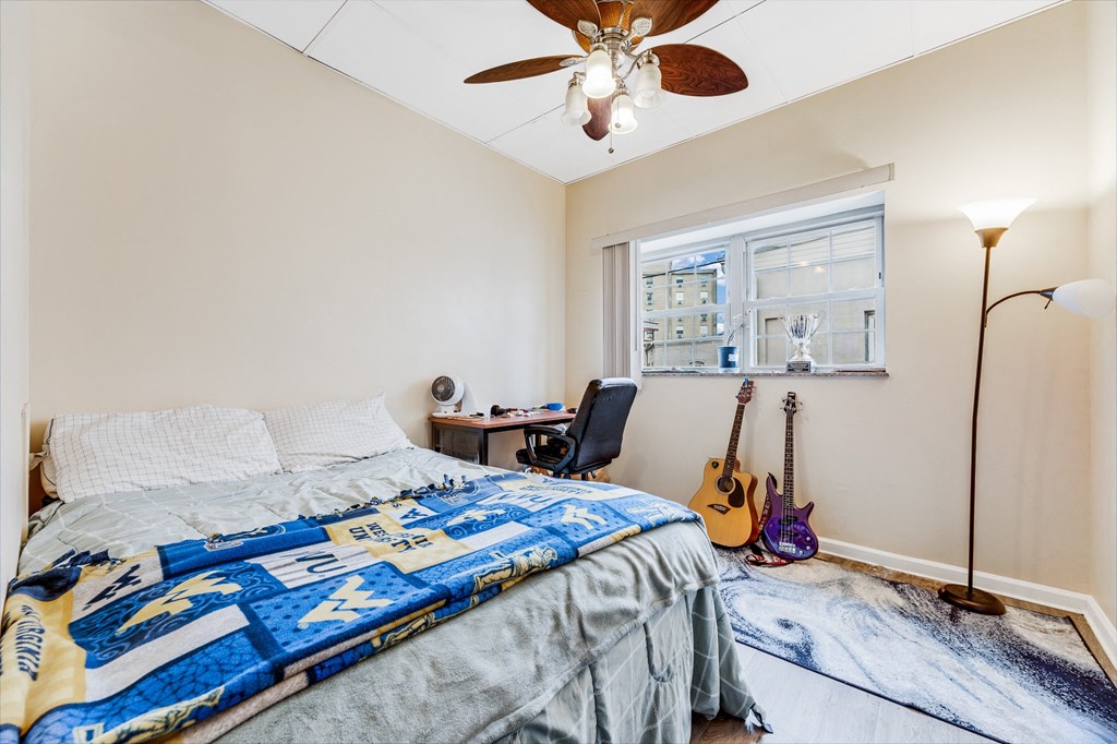 A bedroom with a bed, a guitar, a desk, and a ceiling fan.