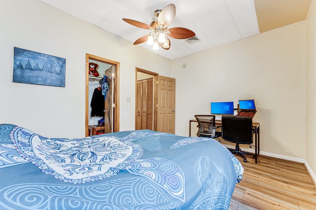 A bedroom with a bed, desk, and ceiling fan.