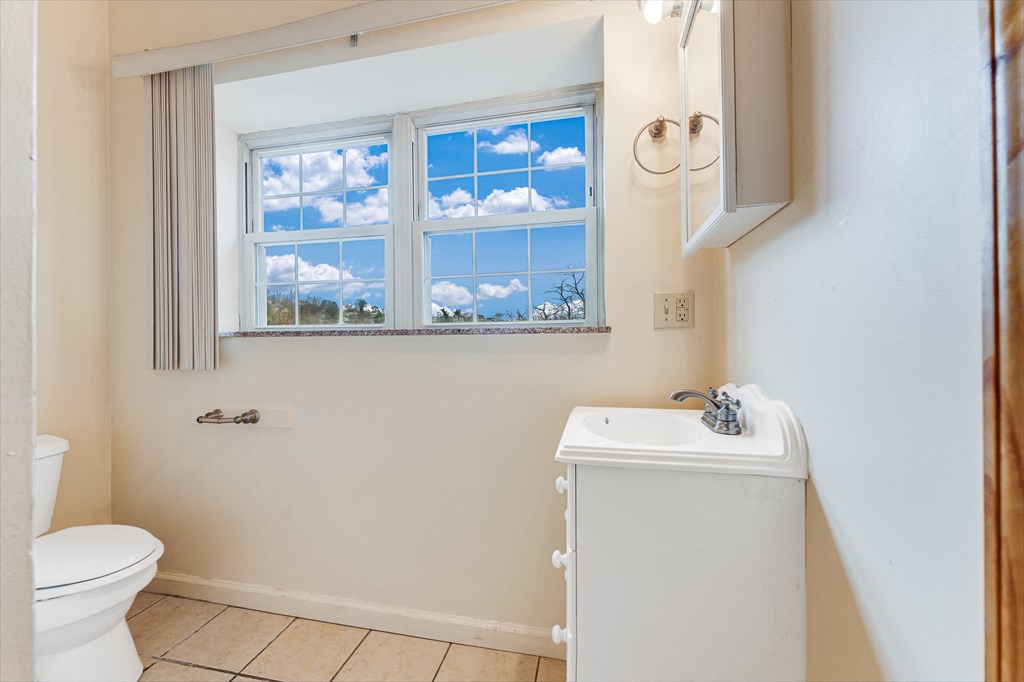 A bathroom with a toilet, sink, and a window with a view of the sky.