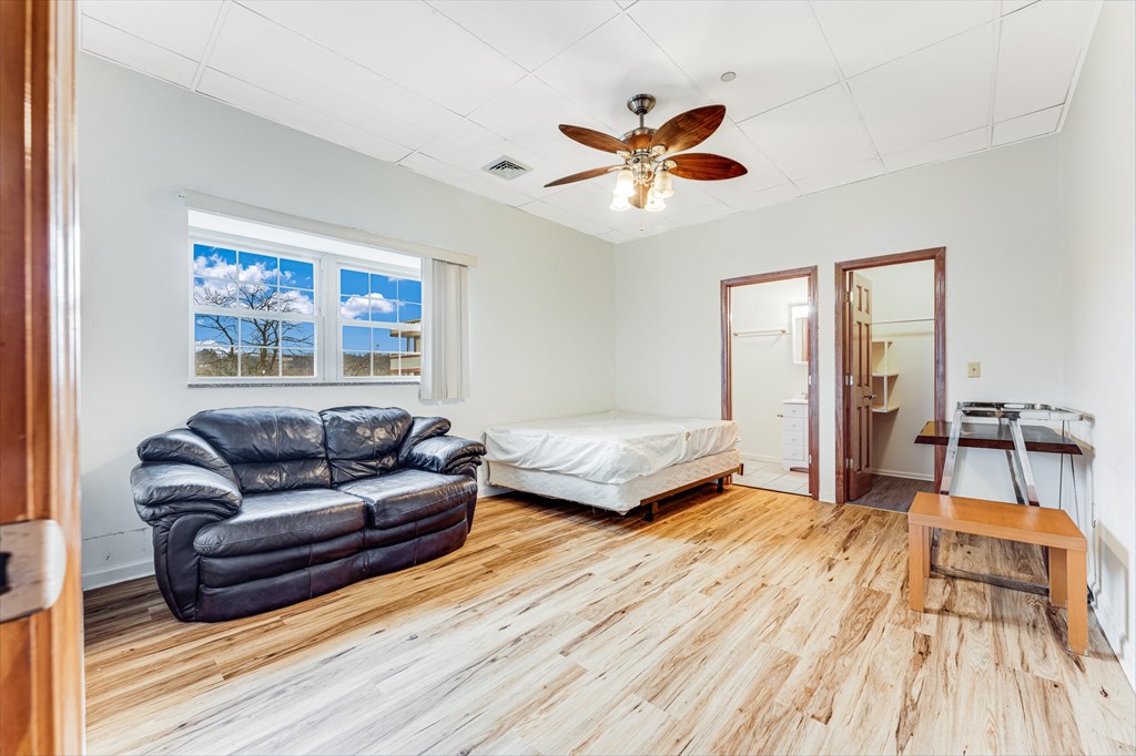 A room with a black leather couch, a bed, and a wooden floor.