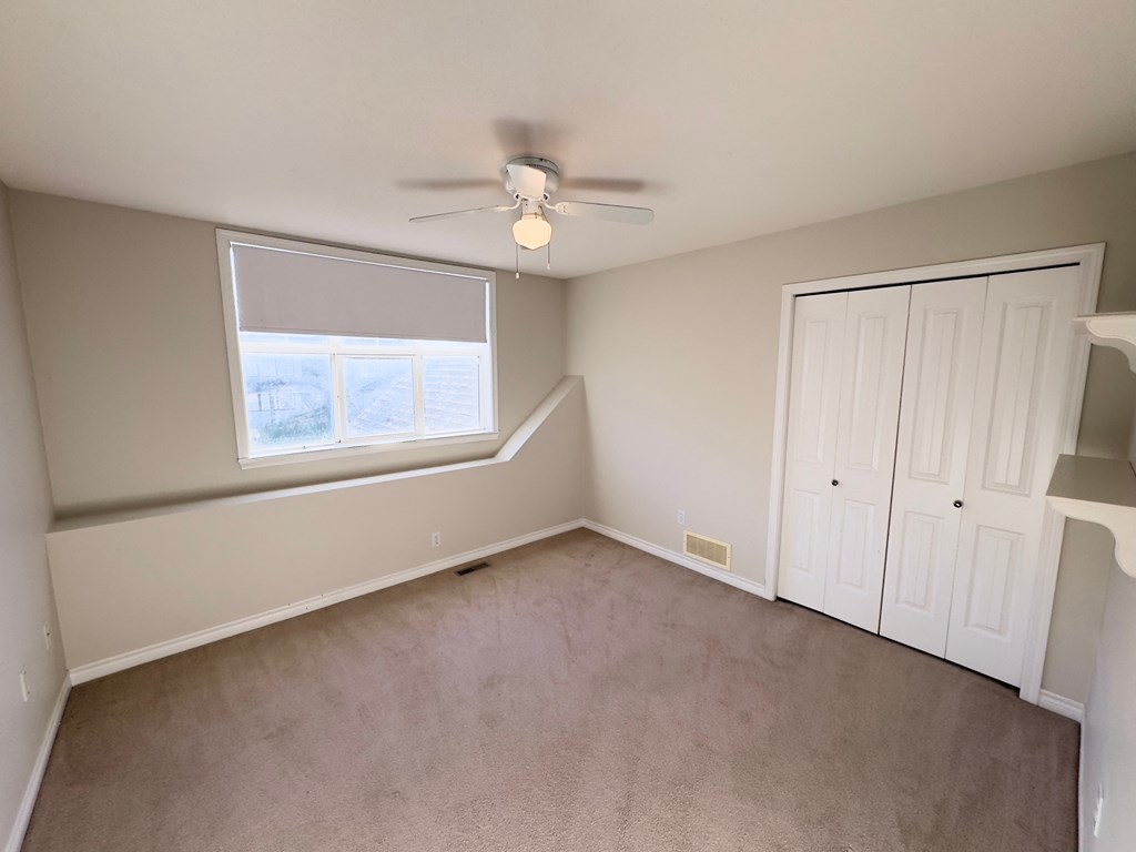 A room with a ceiling fan and a window with blinds.