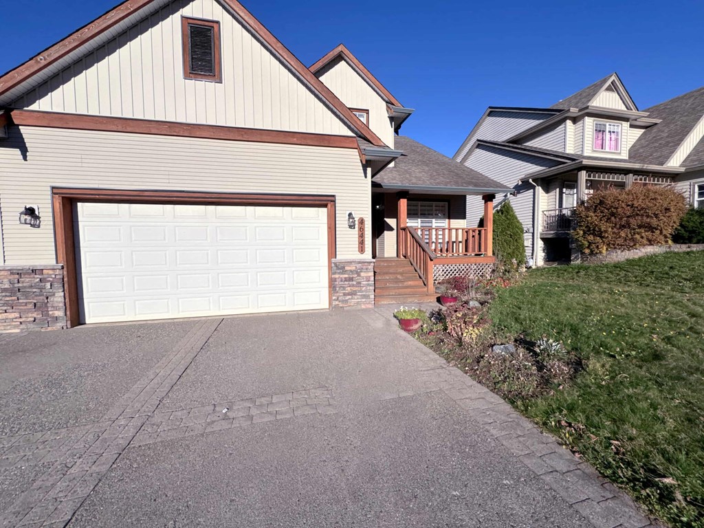 A house with a white garage door is in front of a house with a brown roof.