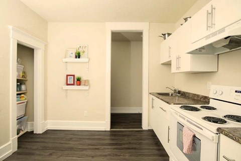 A kitchen with a white stove top oven and white cabinets.