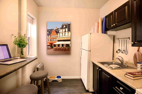 A kitchen with a white refrigerator and a painting of a building on the wall.