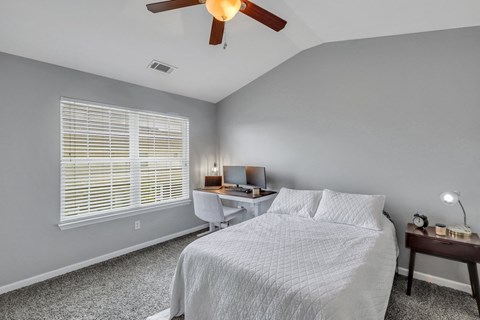 A bedroom with a bed, desk, and window with blinds.