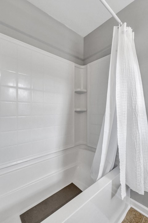 A white shower curtain hangs over a white bathtub.
