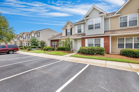 A row of houses with a red car parked in the parking lot.