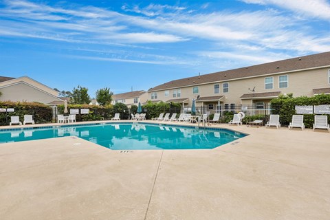 A swimming pool surrounded by lounge chairs in front of apartment buildings.
