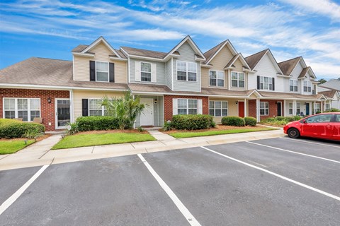A red car is parked in a parking lot in front of a building.