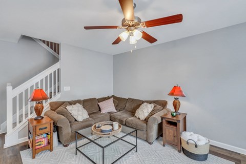 A living room with a brown couch, a glass coffee table, and a ceiling fan.