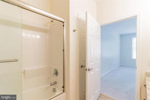 A bathroom with a glass shower door and a white door leading to a bedroom.
