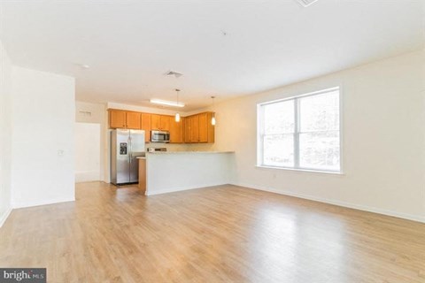 A spacious living room with wooden floors and a kitchen area in the background.