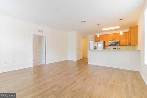 A spacious living room with wooden floors and a kitchen area in the background.