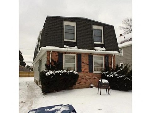 A house with a black roof and a brick chimney is surrounded by snow.