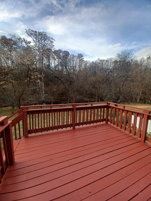A red wooden deck with a railing and trees in the background.