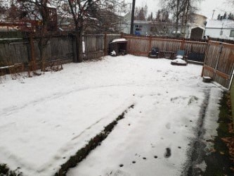 A snow-covered backyard with a wooden fence.