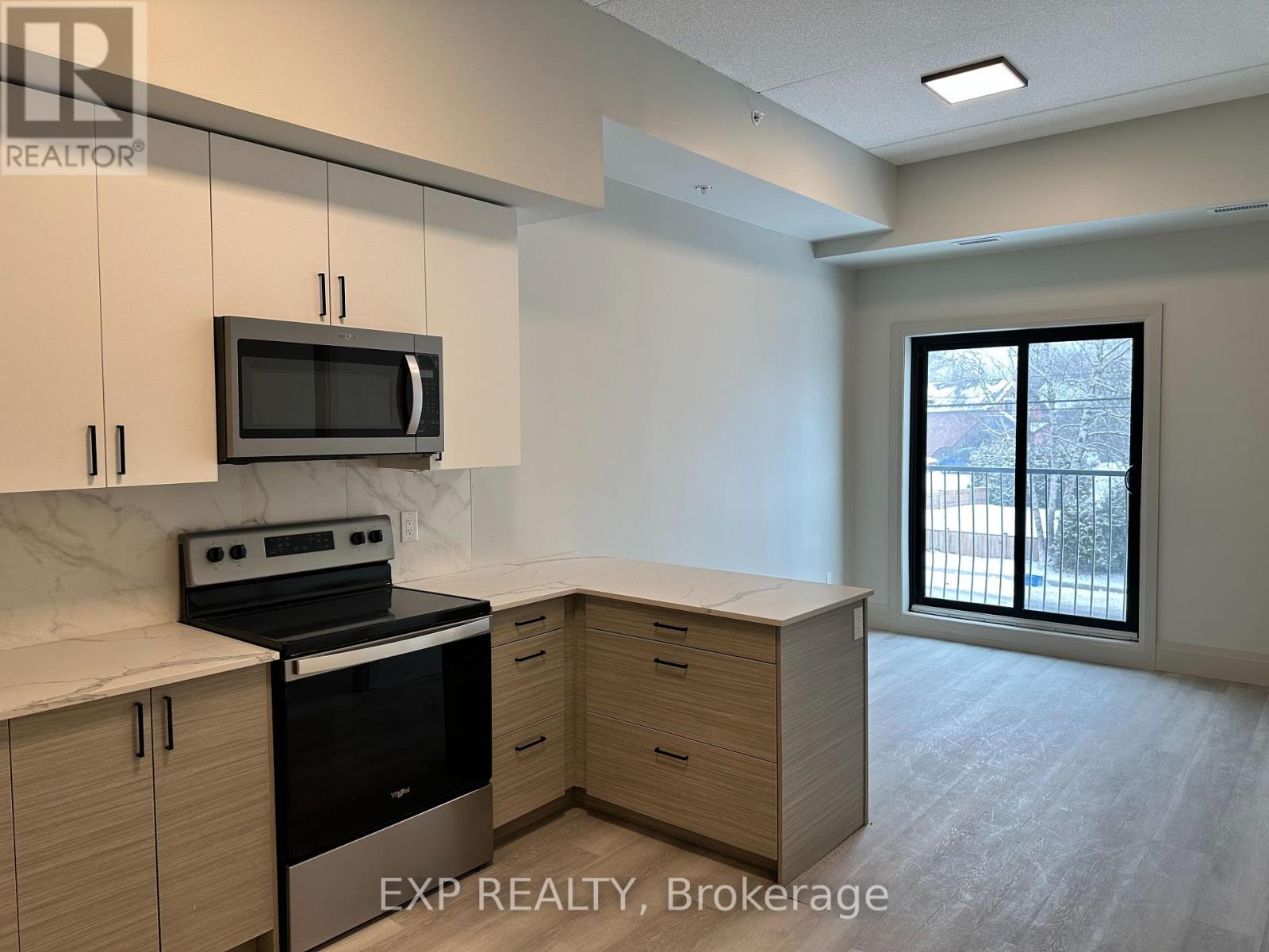 A kitchen with a black stove and microwave, wooden cabinets, and a sliding glass door leading to a balcony.