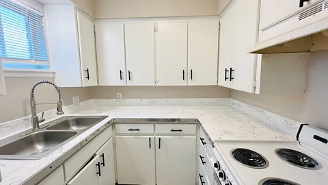 A kitchen with white cabinets and a white stove top oven.