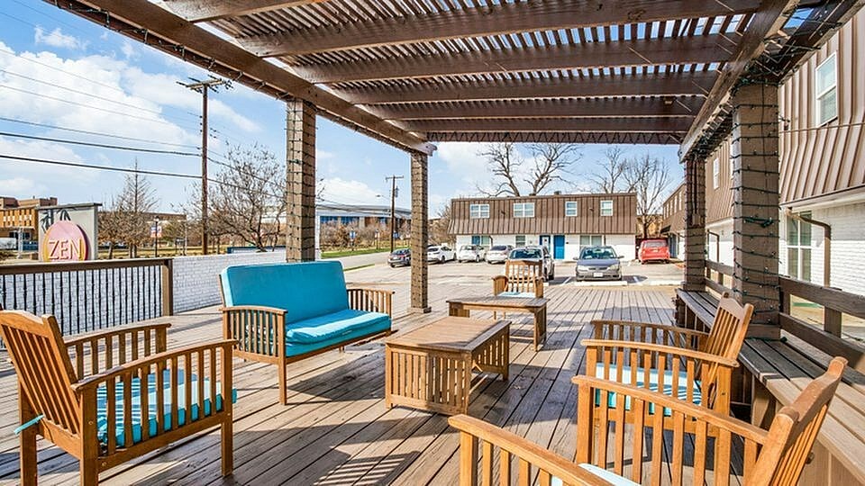 A wooden deck with a blue couch and chairs under a roof.