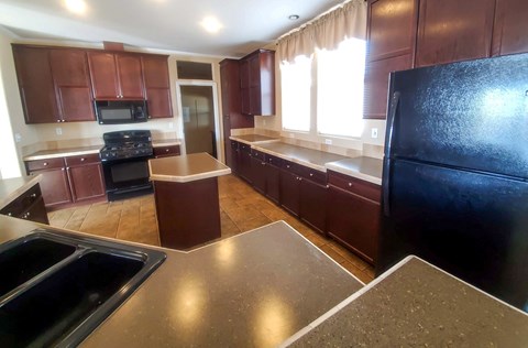 A kitchen with brown cabinets and a black refrigerator.