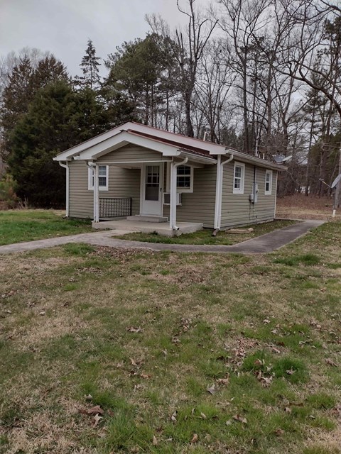 A small house with a porch is surrounded by a grassy area and trees.