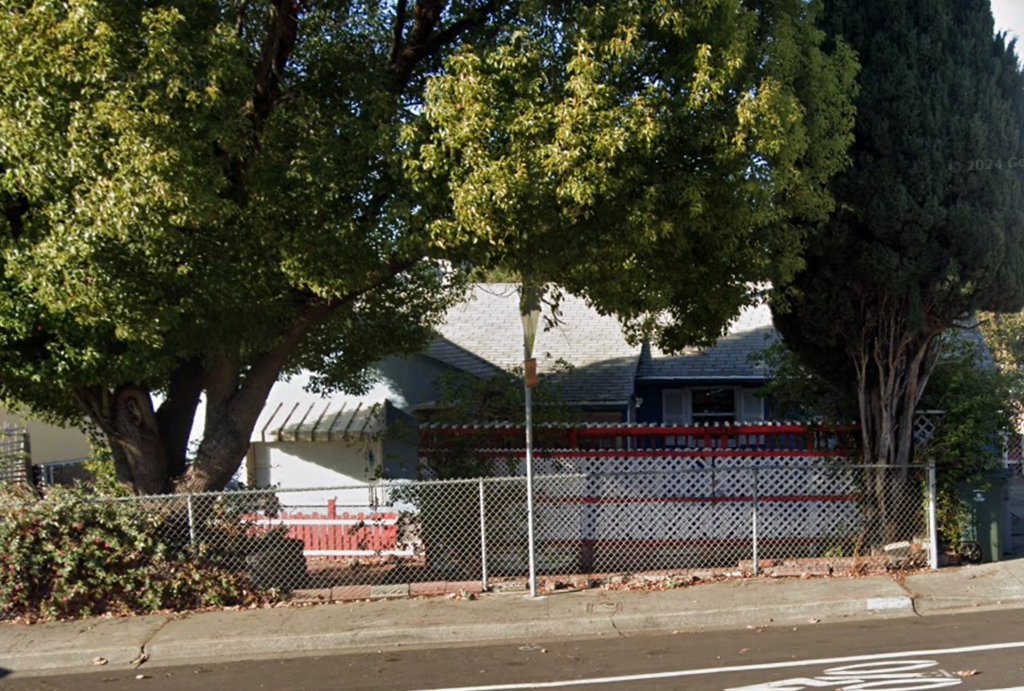 A tree in front of a house with a fence.