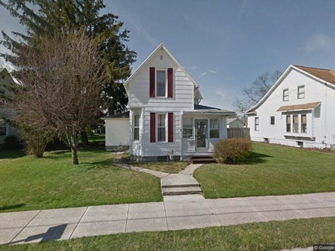 A white house with a red door and a tree in front.