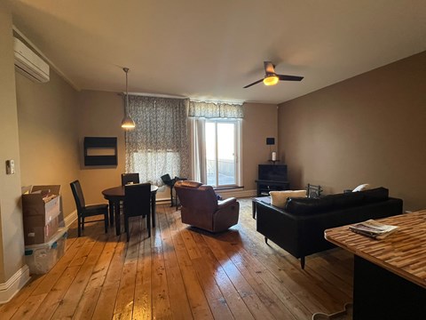 A living room with a black couch, a wooden table, and a window with curtains.