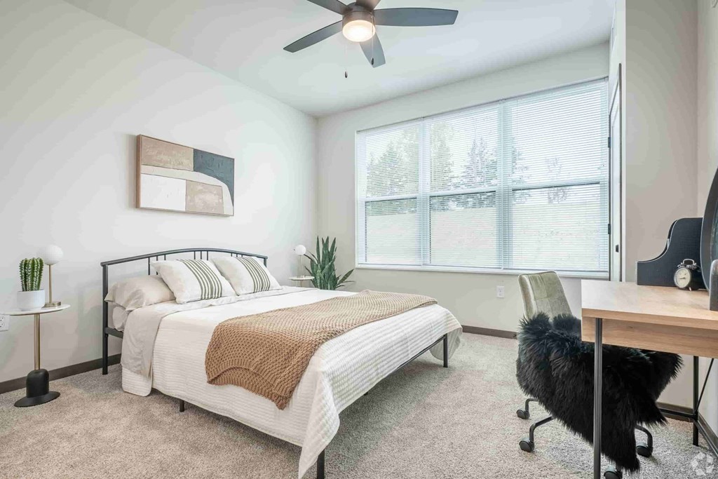 A bedroom with a bed, a chair, a desk, and a ceiling fan.