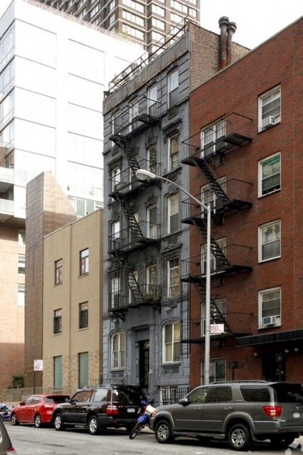 A grey car is parked on the street in front of a building with a fire escape.