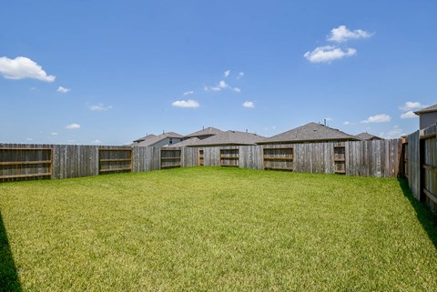 A large grassy field with a wooden fence and houses in the background.