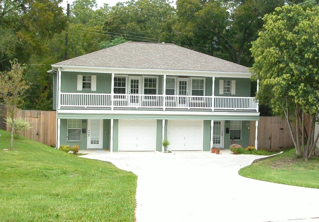 A green house with a grey roof and a white fence.